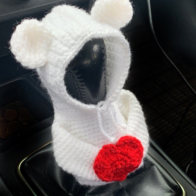 May include: White crocheted bear-shaped car gear shift cover with a red crocheted heart on the front.