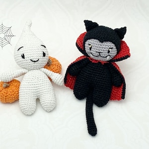 May include: A white crocheted ghost holding two orange pumpkins and a black crocheted cat wearing a red cape with fangs.
