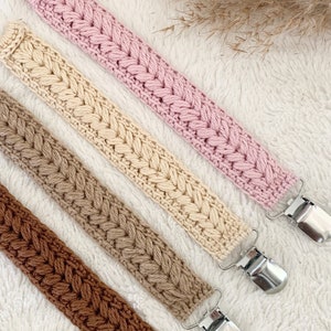 May include: Four crocheted pacifier clips in pink, beige, brown, and a darker brown. Each clip has a silver metal clip on the end.