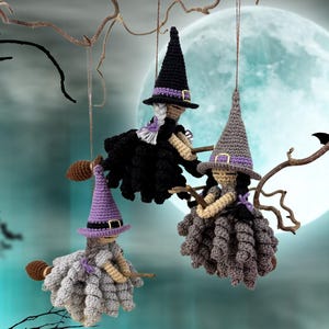 May include: Three crocheted witch ornaments hanging from a branch. Each figure wears a pointed hat with a purple band and buckle, has yarn hair, and holds a small wooden broomstick. The dresses are textured in black, gray, and light gray.