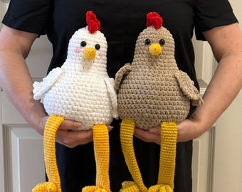 May include: Two crocheted chicken plushies. One is white, the other is brown. Both have red combs, yellow beaks and legs. The white chicken has pink cheeks. The chickens are handmade and have a whimsical design.