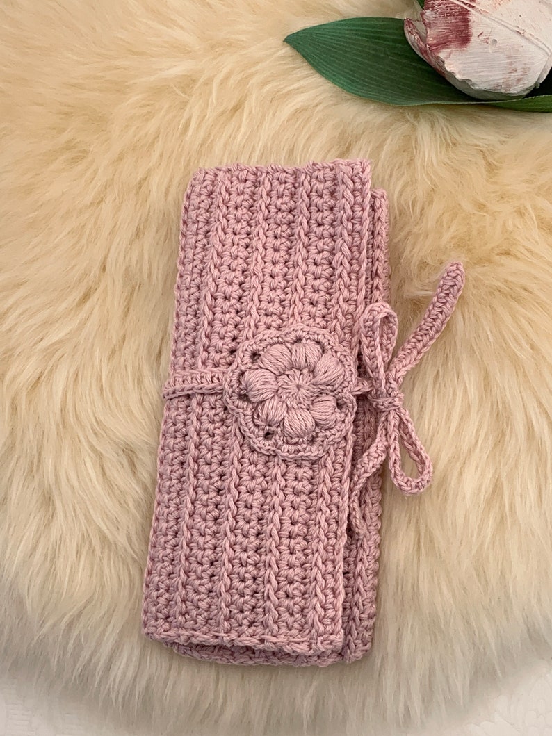 Puede incluir: Una manta de ganchillo rosa con un dise&ntilde;o de flores y un cierre de lazo.