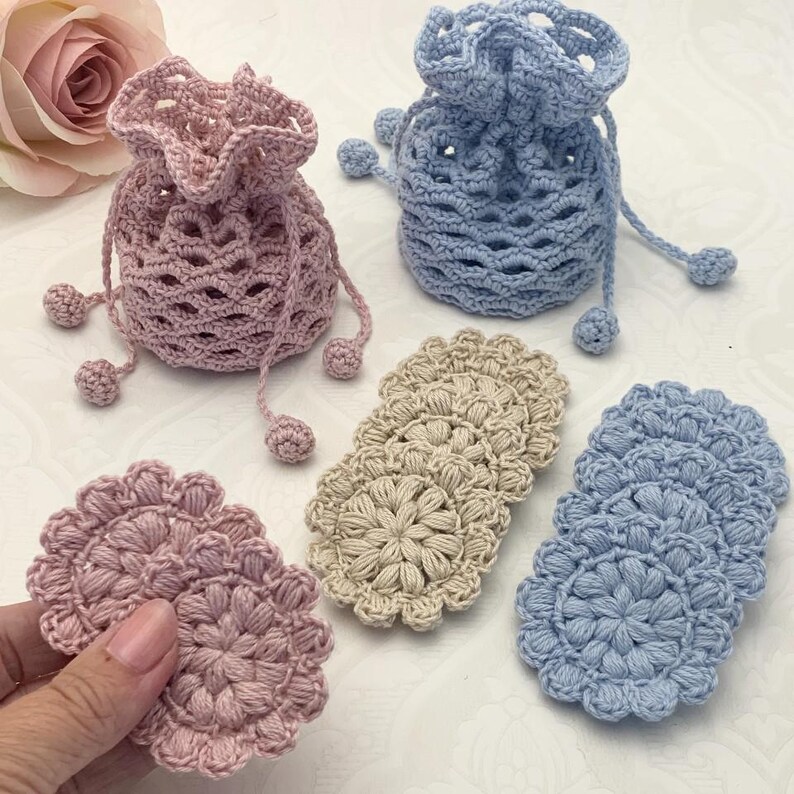 Puede incluir: Conjunto de art&iacute;culos de ganchillo que incluye dos bolsas de cord&oacute;n, una rosa y otra azul, y seis posavasos de ganchillo en rosa, azul y beige.