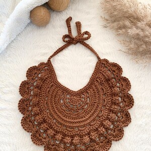 May include: A brown crocheted bib with a scalloped edge and a bow at the top.
