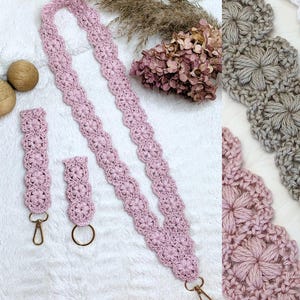 May include: A set of crochet accessories in a dusty pink hue, featuring a long lanyard and two shorter wristlet straps. Each piece is crafted with a repeating floral motif and finished with gold-toned metal lobster clasps and a circular ring.