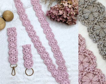 May include: A set of crochet accessories in a dusty pink hue, featuring a long lanyard and two shorter wristlet straps. Each piece is crafted with a repeating floral motif and finished with gold-toned metal lobster clasps and a circular ring.