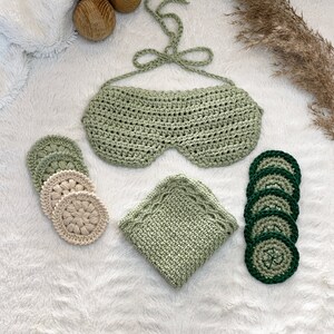 May include: A set of crocheted items in green and white, including a sleep mask, a washcloth, and four round coasters. The coasters are green with a white center.