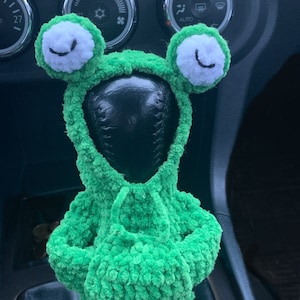 Pu&ograve; includere: Copri leva del cambio in crochet verde a forma di rana con occhi bianchi e bocca nera. La copertura &egrave; sulla leva del cambio di un'auto.