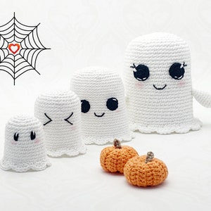 May include: Four crocheted ghost ornaments with smiling faces and black eyes. Two orange crocheted pumpkins are in the foreground.