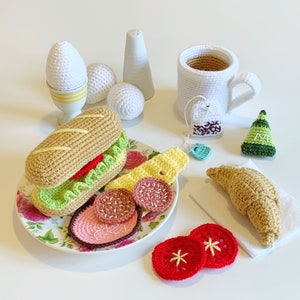 May include: A crocheted breakfast set with a sandwich, croissant, eggs, tea bag, and fruit. The set is made of yarn and is a fun and whimsical way to play pretend.