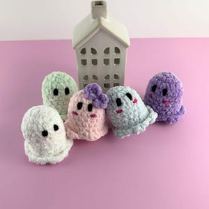 Puede incluir: Una colecci&oacute;n de cinco peluches de fantasmas hechos a mano con ganchillo en varios colores pastel, incluyendo blanco, verde menta, rosa, azul claro y morado. Cada fantasma tiene ojos negros y una boca sonriente. Una casa de cer&aacute;mica blanca est&aacute; en el fondo.
