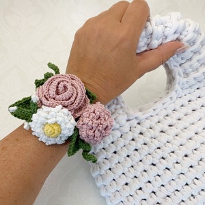 May include: A crocheted flower bracelet with pink and white flowers and green leaves.