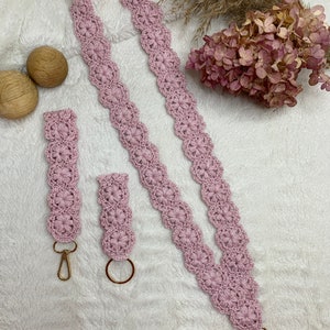 May include: A set of two pink crocheted keychains with gold key rings. The longer keychain is a lanyard style and the shorter keychain is a simple loop.