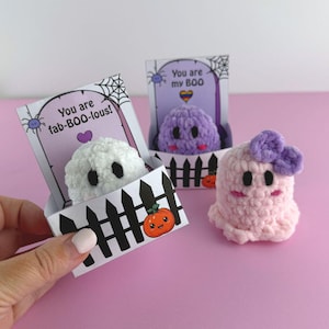 Könnte beinhalten: Drei gehäkelte Geisterfiguren im Halloween-Thema. Ein weißer Geist befindet sich in einer schwarz-weißen Zaunkiste mit dem Text "You are fab-BOO-lous!". Ein lila Geist befindet sich in einer ähnlichen Kiste mit dem Text "You are my BOO". Ein rosa Geist mit einer lila Schleife ist ebenfalls vorhanden.