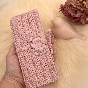 Puede incluir: Una bolsa de crochet rosa con un dise&ntilde;o de flores y un cierre de corbata.