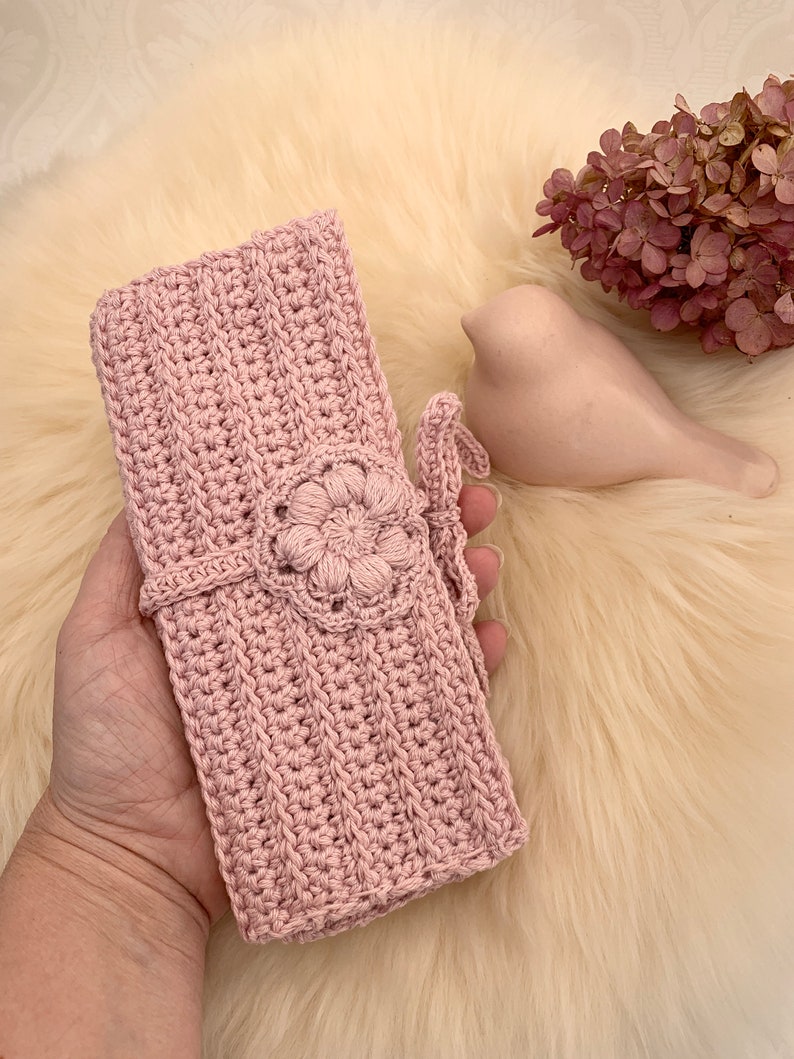 Puede incluir: Una bolsa de crochet rosa con un dise&ntilde;o de flores y un cierre de corbata.