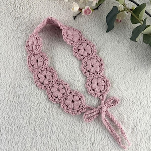 Puede incluir: Una diadema de ganchillo rosa empolvado con un diseño floral. La diadema está adornada con múltiples flores de ganchillo y tiene un lazo al final para atar. El artículo es hecho a mano y adecuado para varias ocasiones.