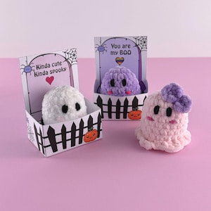 Puede incluir: Tres figuras de fantasmas de ganchillo hechas a mano. Un fantasma blanco en una caja con el texto "Kinda cute Kinda spooky". Un fantasma morado en una caja con el texto "You are my BOO". Un fantasma rosa con un lazo morado.