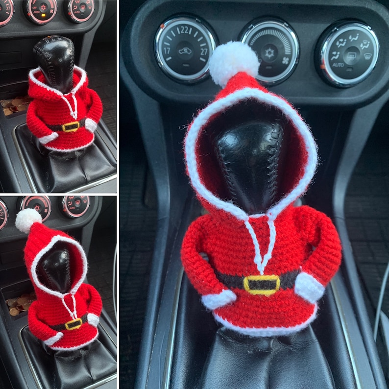 Puede incluir: Una figura de Pap&aacute; Noel de crochet en rojo y blanco, con un gorro blanco con pomp&oacute;n, se coloca en la palanca de cambios de un coche.
