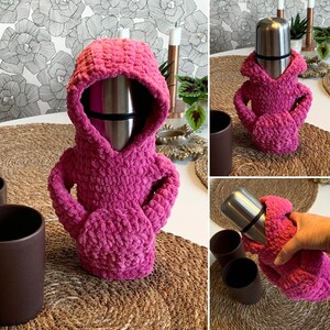 May include: A pink crocheted hoodie for a thermos or water bottle. The hoodie is made with a soft, fuzzy yarn and has a drawstring hood. The thermos is silver and has a black lid.