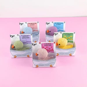 Puede incluir: Cuatro peque&ntilde;os patos de crochet en diferentes colores, cada uno en una caja de ba&ntilde;era blanca con un mensaje diferente en el frente. Los mensajes son: "You make me feel so ducky!" "In a world full of pigeons be a fabulous DUCK!" "I ducking Love you!" y "If life gives you lemons be a DUCK!"