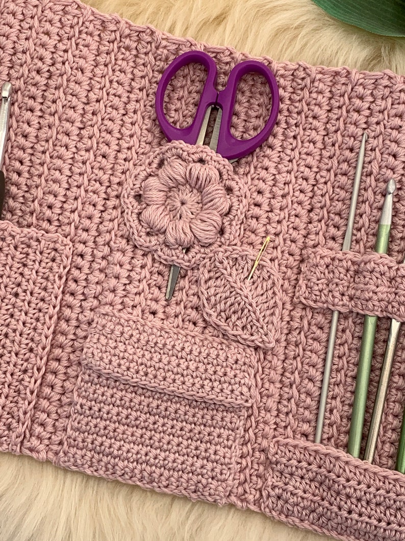 Puede incluir: Un estuche para agujas de crochet de color rosa con varios bolsillos y ranuras para guardar agujas de tejer, ganchos de crochet, tijeras y otras herramientas. El estuche tiene un dise&ntilde;o de flor y hoja de crochet.