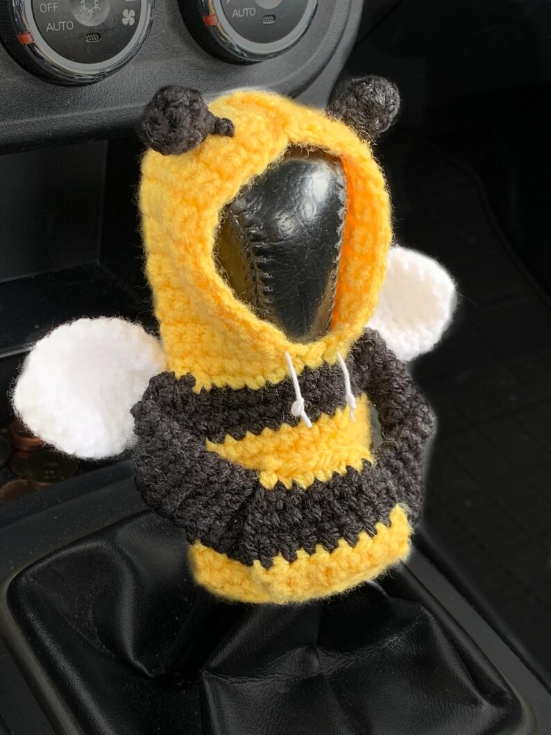 Peut inclure: Un couvre-levier de vitesse en crochet en forme d'abeille, jaune, noir et blanc. L'abeille a un corps ray&eacute; noir et jaune, des ailes blanches et une t&ecirc;te noire &agrave; capuche.
