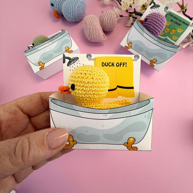 Puede incluir: Un pato amarillo de crochet en una ba&ntilde;era con interior azul y blanco. La ba&ntilde;era es parte de una tarjeta que dice "Duck Off!" con una toalla amarilla.