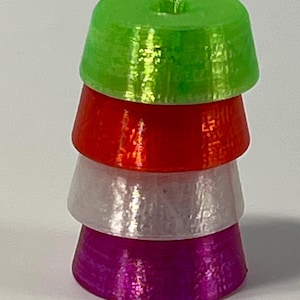 May include: A stack of four colorful, cone-shaped objects. The top is bright green, followed by red, silver, and purple. Each cone has a slightly textured surface and a small hole at the top. The objects are stacked on top of each other.