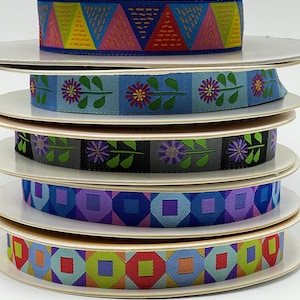 May include: Five spools of colorful patterned ribbon. The ribbons are stacked on top of each other. The top ribbon is pink, yellow, and red with a geometric pattern. The second ribbon is blue with a floral pattern. The third ribbon is gray with a floral pattern. The fourth ribbon is purple and blue with a geometric pattern. The bottom ribbon is green, blue, and red with a geometric pattern.