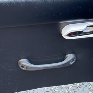 Peut inclure: Gros plan sur un panneau de porte de voiture noir avec une poignée grise et un cadre de poignée de porte blanc. Le cadre de la poignée de porte entoure une poignée de porte noire avec un bouton rouge.
