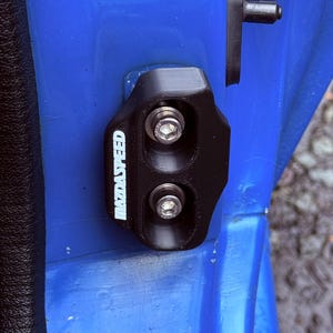May include: A black plastic door handle with the words "MazdaSpeed" in white lettering. The handle is attached to a blue car door.