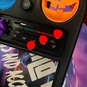 Peut inclure: Un tableau de bord de voiture noir avec un couvercle de ventilation en forme de citrouille. Le tableau de bord a un autocollant qui dit "Just Do It" et un autocollant avec un design graphique. Il y a quatre boutons en forme de crâne rouge sur le tableau de bord.