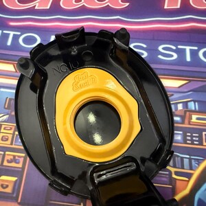 May include: A black and yellow automotive component featuring the text "Just Send It". The part has a circular shape with a central aperture and several projecting tabs.