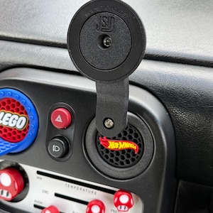 Könnte beinhalten: Schwarzes Armaturenbrett mit einer magnetischen Telefonhalterung und roten, pilzförmigen Knöpfen. Ein Hot Wheels-Logo ist auf der Lüftung zu sehen, und ein LEGO-Logo befindet sich links. Die Telefonhalterung trägt die Aufschrift "MAGNETIC HOLDER".