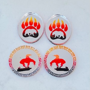May include: Four round, silver-colored, decorative, acrylic ornaments. Two ornaments feature a red, orange, and yellow bear paw print with a black bear silhouette. Two ornaments feature a red, orange, and yellow Native American design with a black silhouette of a person riding a horse.