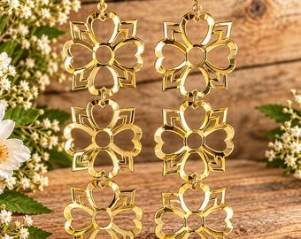May include: A pair of gold-toned dangle earrings, each featuring three vertically aligned, openwork flower motifs. The design consists of symmetrical, heart-shaped petals arranged in a square frame, suspended from simple gold-toned earring hooks.