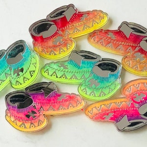 Op de afbeelding: Acht kleurrijke, gespiegelde, decoratieve mocassins met een geometrisch patroon. De mocassins zijn in tinten rood, oranje, geel, groen, blauw en paars.