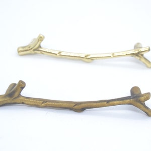 Può includere: Due tiretti per mobili in metallo color oro a forma di rami. I tiretti hanno un aspetto rustico e naturale.