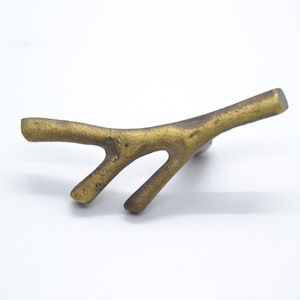 May include: A gold-toned metal cabinet knob shaped like a branch with three points.
