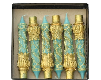 May include: A box of six teal and gold decorative candles. The candles have a detailed, ornate design.