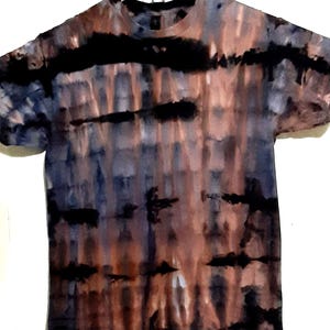 Puede incluir: Una camiseta teñida con tintes en tonos marrón, azul y negro. La camiseta tiene cuello redondo y mangas cortas. El patrón teñido anudado presenta bandas negras horizontales y vetas verticales de color.