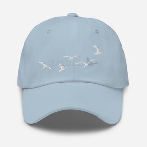 May include: A light blue baseball cap with white embroidered birds flying in formation. The text "The Anchor & Bird" and a website address are also embroidered on the cap.