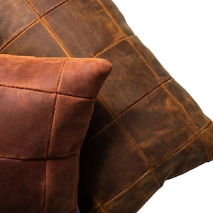 May include: Two brown leather pillows with a quilted design. The pillows are made of different shades of brown leather and have a rustic look.