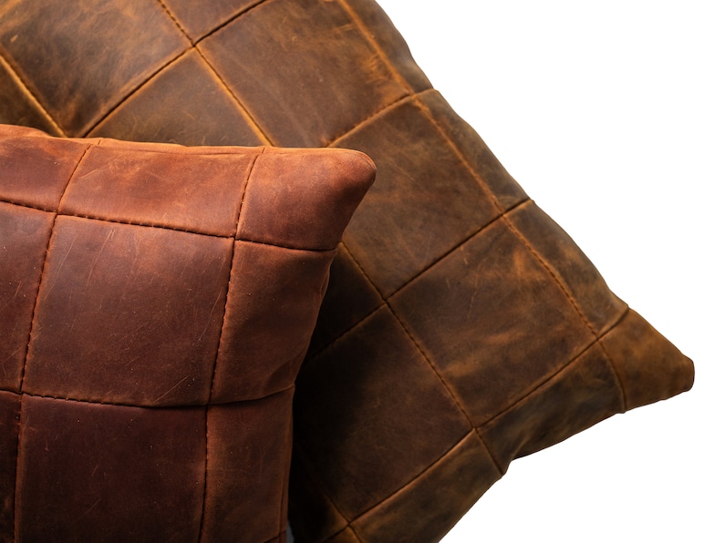 May include: Two brown leather pillows with a quilted design. The pillows are made of different shades of brown leather and have a rustic look.