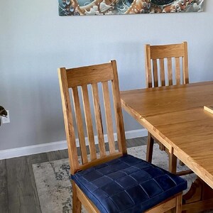 K&ouml;nnte beinhalten: Ein Esstisch aus Holz mit einer hellen Holzoptik und einem blau gepolsterten Stuhl. Der Tisch ist rechteckig und aus massivem Holz gefertigt. Der Stuhl hat eine Lattenr&uuml;cklehne und einen gepolsterten Sitz.
