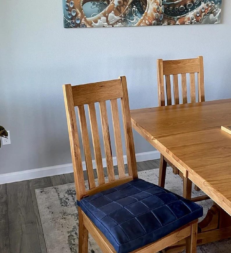K&ouml;nnte beinhalten: Ein Esstisch aus Holz mit einer hellen Holzoptik und einem blau gepolsterten Stuhl. Der Tisch ist rechteckig und aus massivem Holz gefertigt. Der Stuhl hat eine Lattenr&uuml;cklehne und einen gepolsterten Sitz.