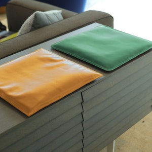 May include: Two leather cushions, one tan and one green, are placed on top of a dark gray wooden cabinet with horizontal slats.