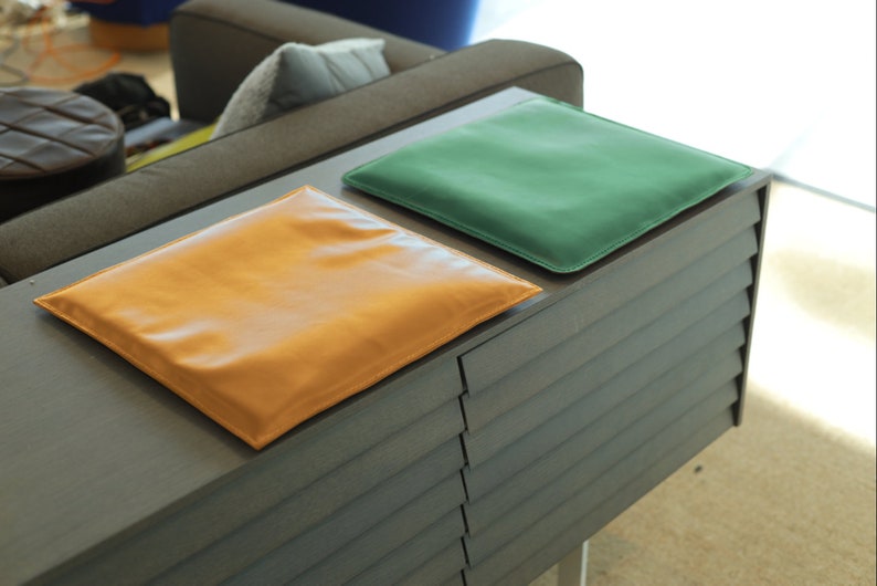 May include: Two leather cushions, one tan and one green, are placed on top of a dark gray wooden cabinet with horizontal slats.