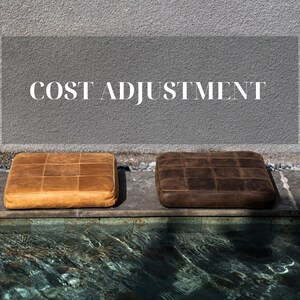 Könnte beinhalten: Zwei quadratische Lederkissen, eines braun und eines beige, liegen auf einer Steinleiste am Rande eines Pools. Der Text "COST ADJUSTMENT" ist in Weiß auf einem grauen Hintergrund über den Kissen geschrieben.